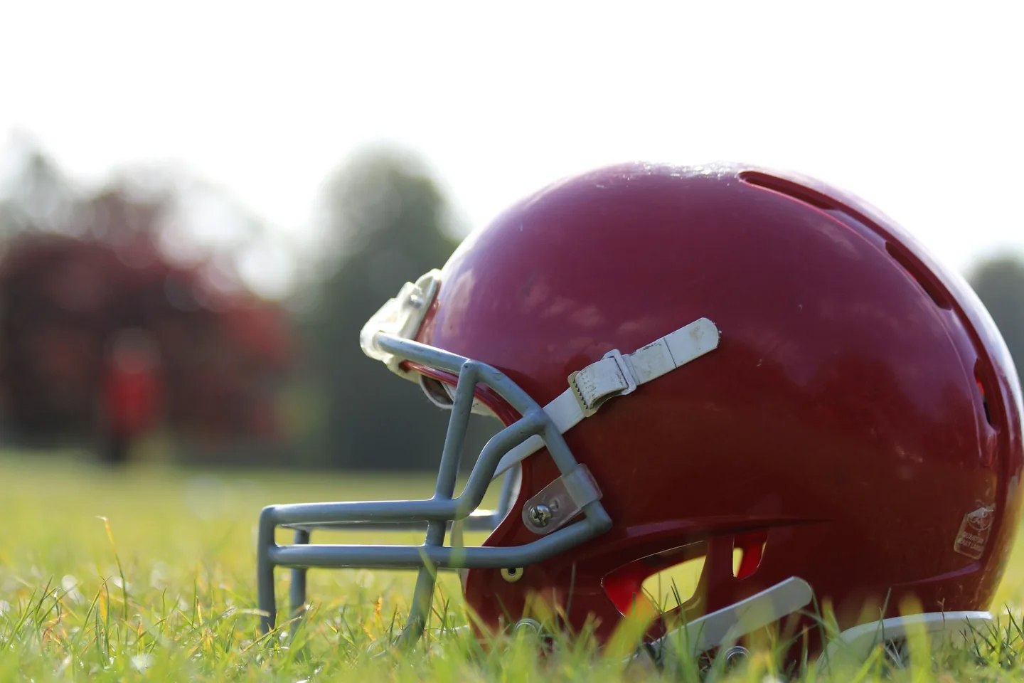 A red football helmet on the grass, a player blurred behind it