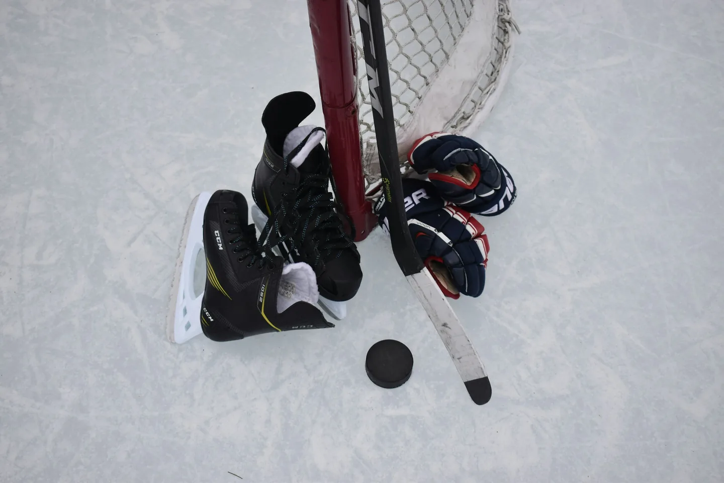 Hockey skates, gloves, a stick and a puck laid out on the ice against the goal post